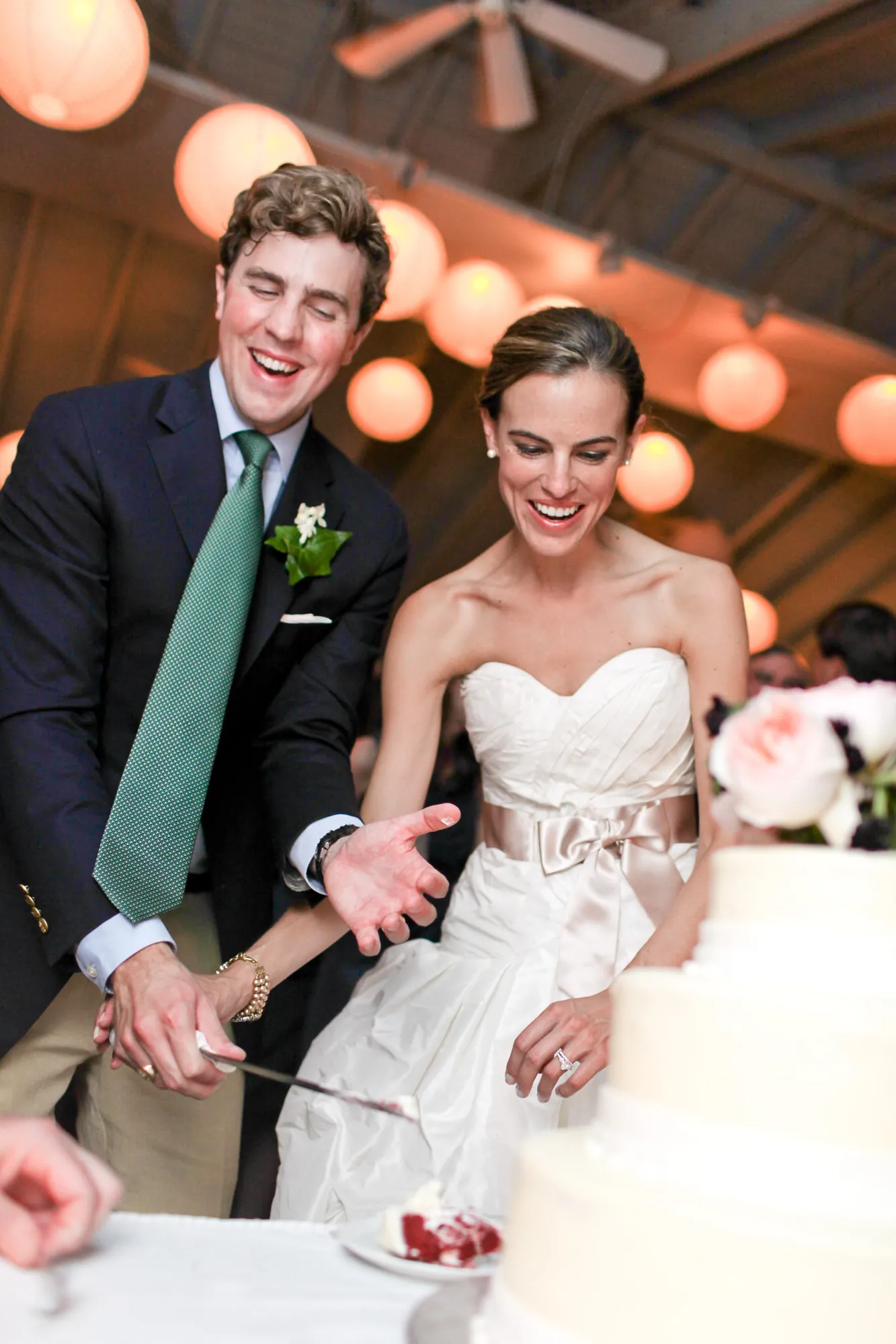 Trevor and Christina laugh as they cut the cake beneath the lanterns