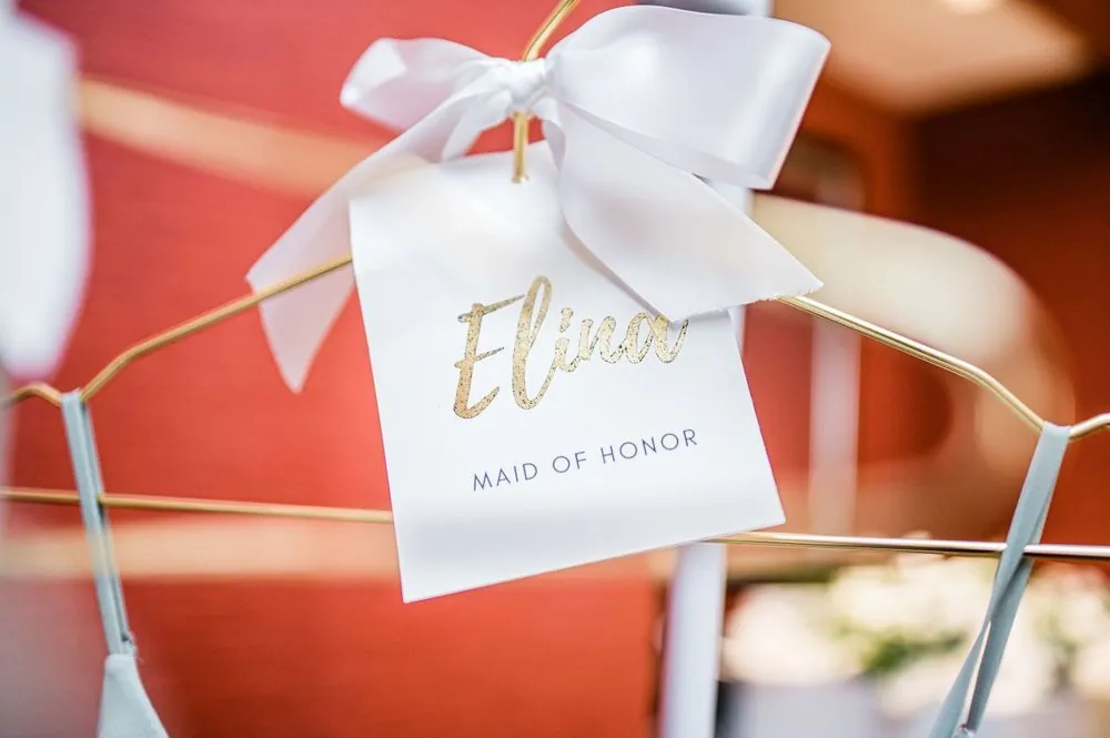A gold maid of honor hanger tag tied with a white ribbon