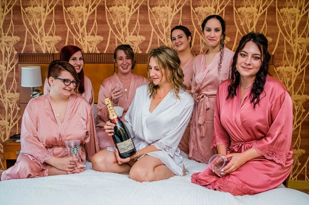 Bridesmaids in pink robes crowd onto the bed around the bride