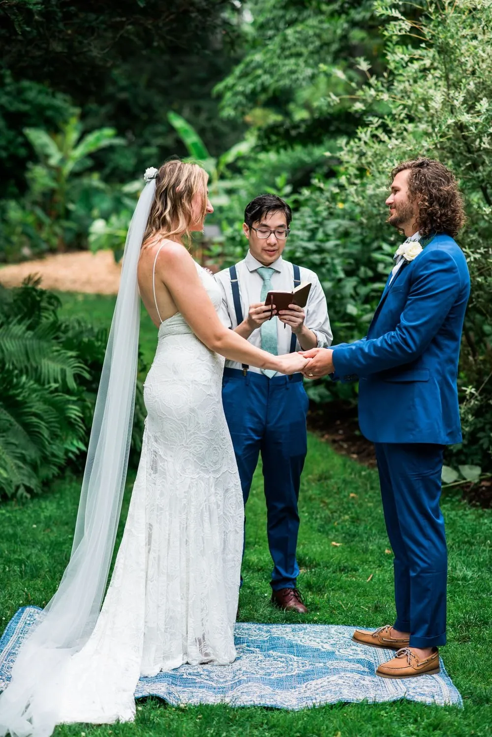 The couple stands facing each other on the lawn with the officiant between them