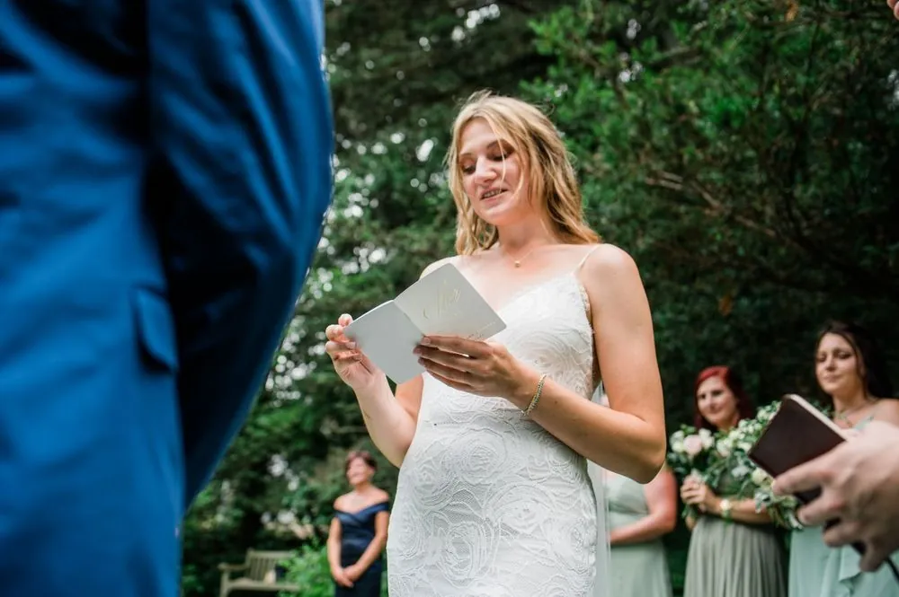 The bride reads her vows from a folded page in the garden