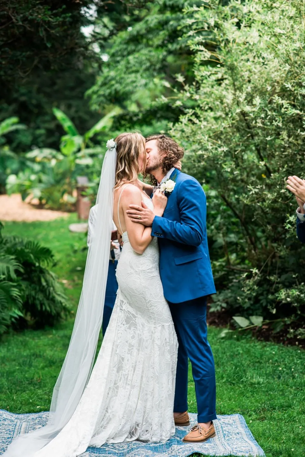 The couple kisses at the end of the ceremony among tall garden trees