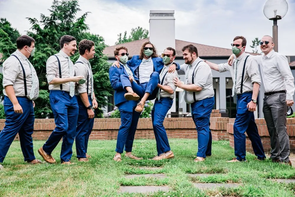 Groomsmen in suspenders goof around with the groom on the lawn