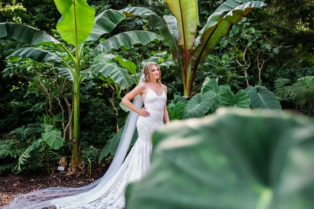The bride stands among giant tropical leaves with her veil trailing