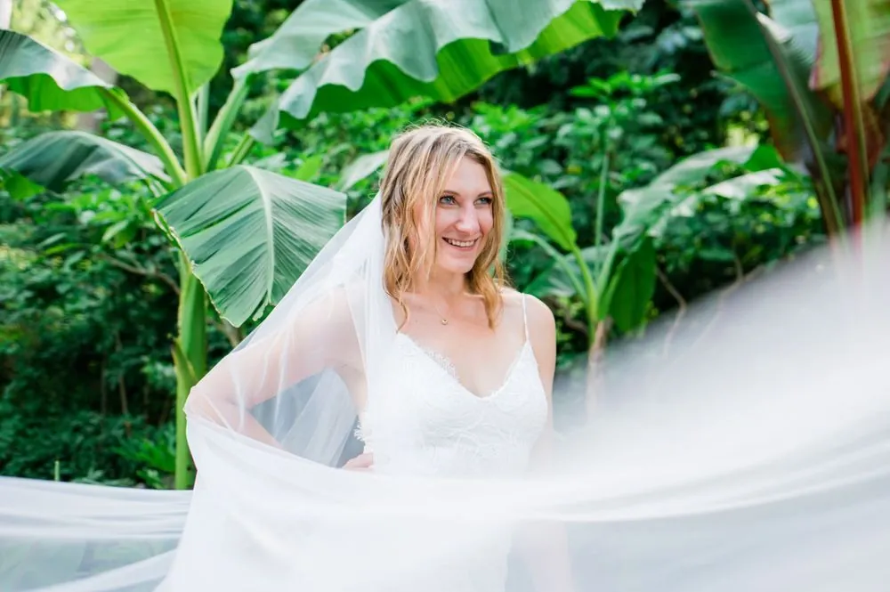 The bride's veil lifts sideways in the air among banana leaves