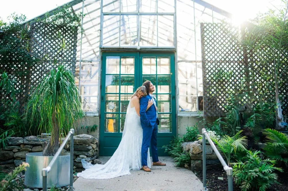 Vita and Mat embrace at the green doors of the old glass greenhouse