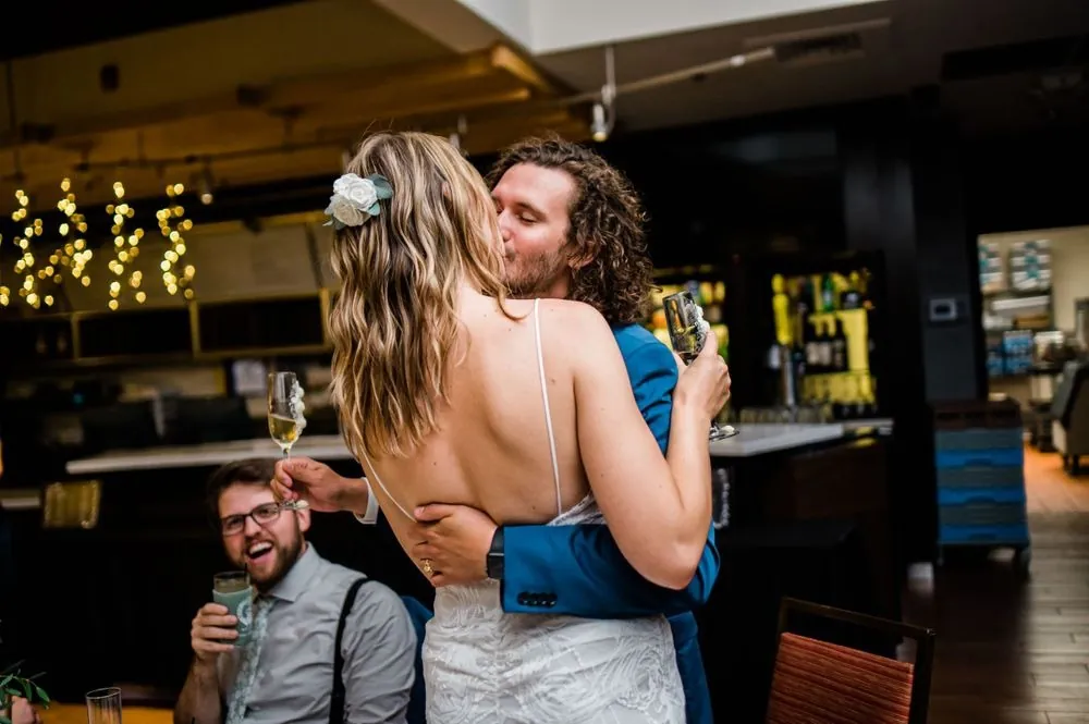 The couple kisses on the dance floor under warm string lights