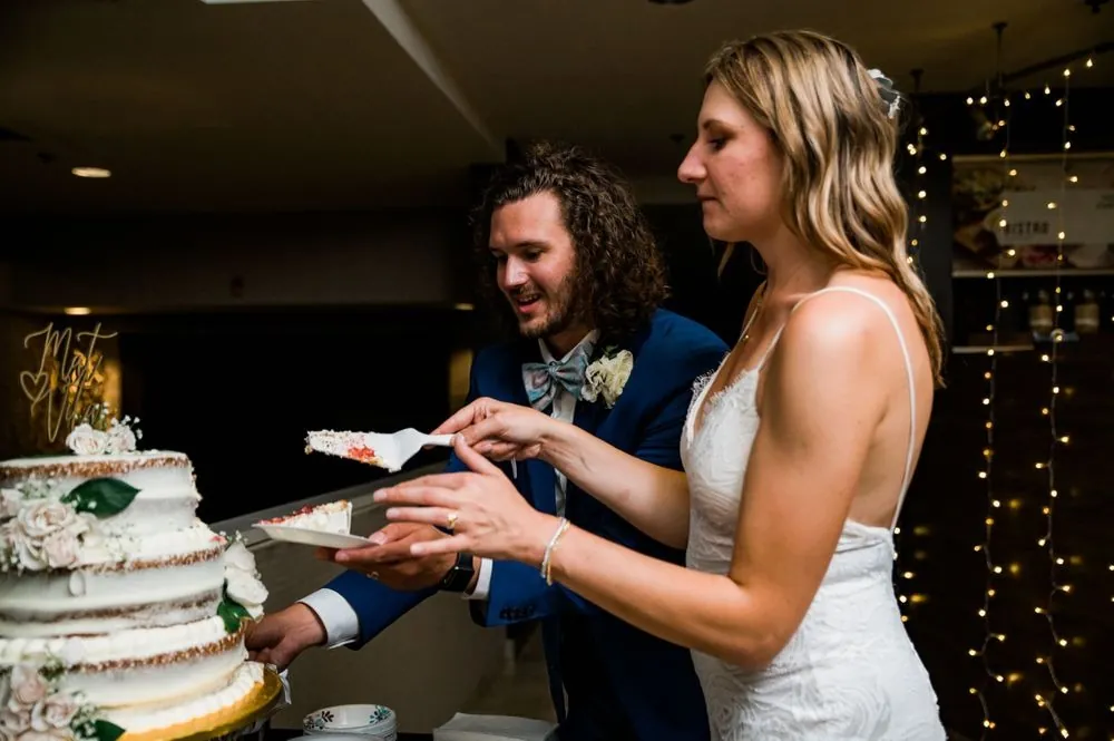 The couple cuts a white cake decorated with green leaves