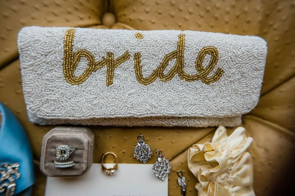 White beaded clutch spelling bride in gold, with ring box and jewelry nearby
