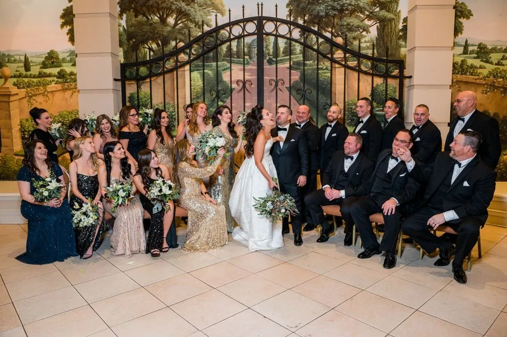 Wedding party in gold sequins, navy, and black tuxedos poses before a painted garden gate