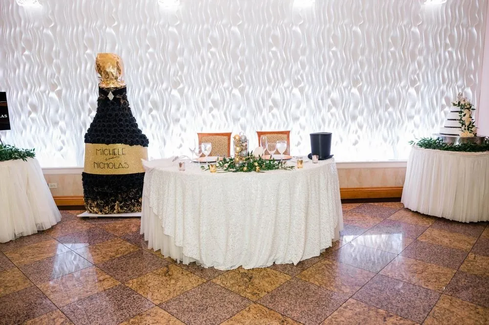 Sweetheart table beside a tall champagne bottle made of black roses with the couple's names