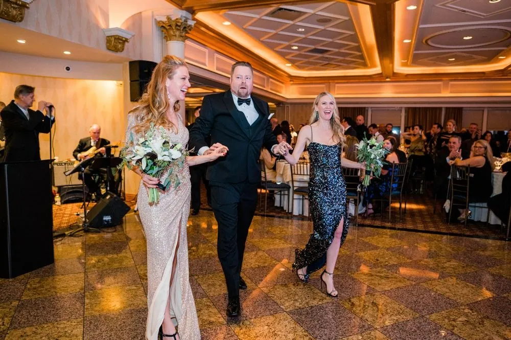 Bridesmaid in a champagne gown walks in on a groomsman's arm as guests watch