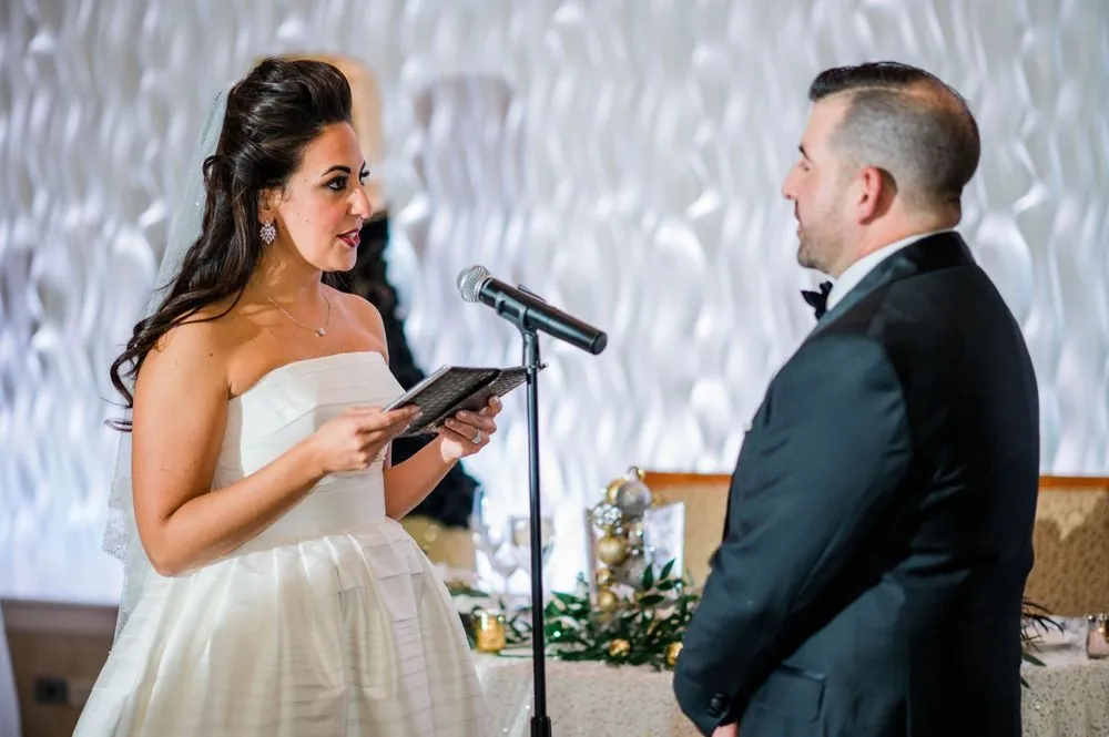 Michele reads her vows into a microphone from a small black book as Nicholas listens