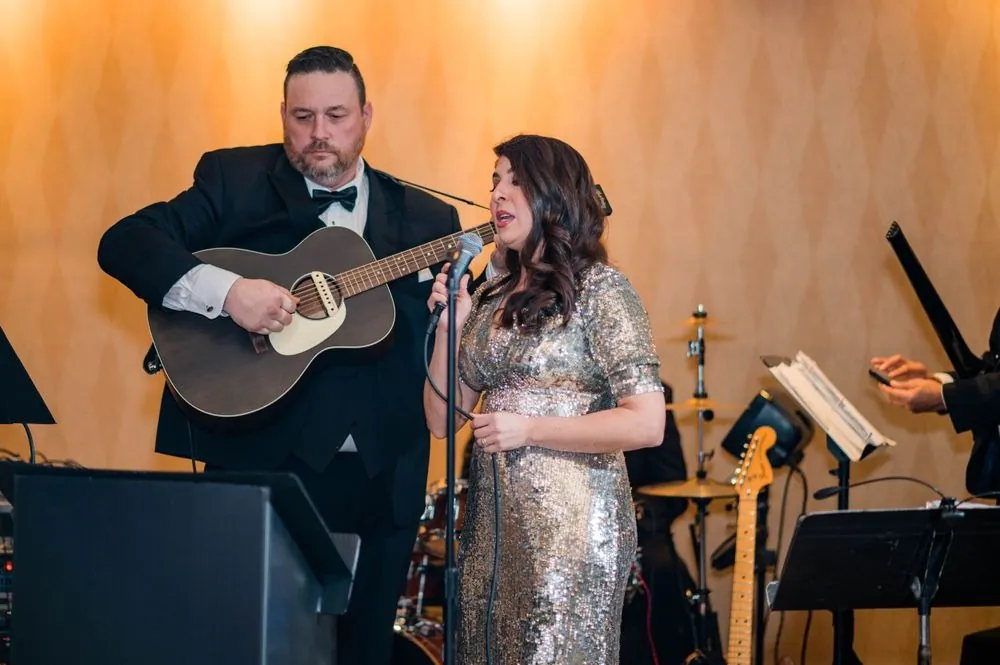 Singer in silver sequins performs beside a guitarist during the reception