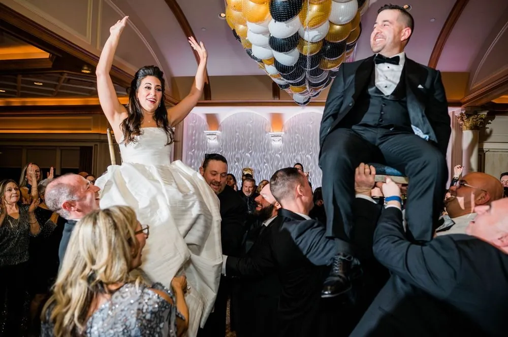 Michele and Nicholas lifted high on chairs beneath a ceiling net of gold and black balloons