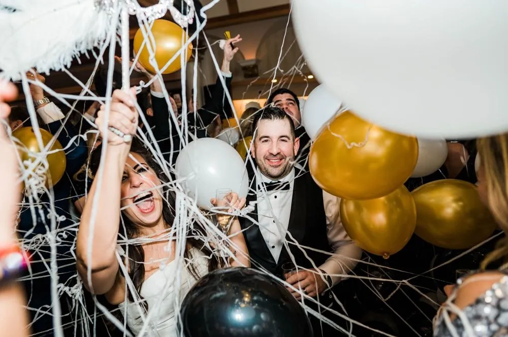 Bride laughs as streamers and gold, white, and black balloons rain down during the balloon drop