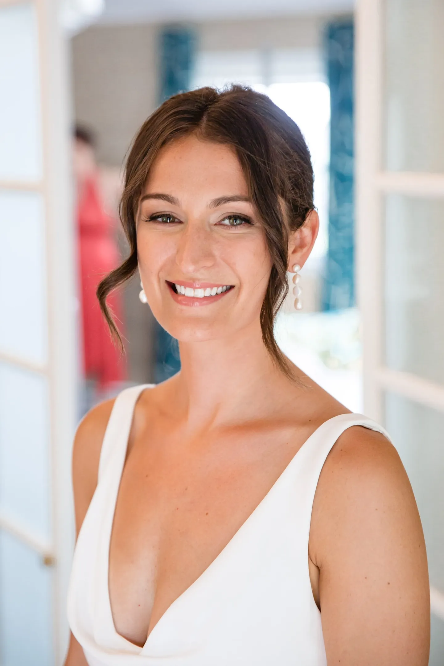 The bride smiles in her plunging white gown by a window with blue shutters
