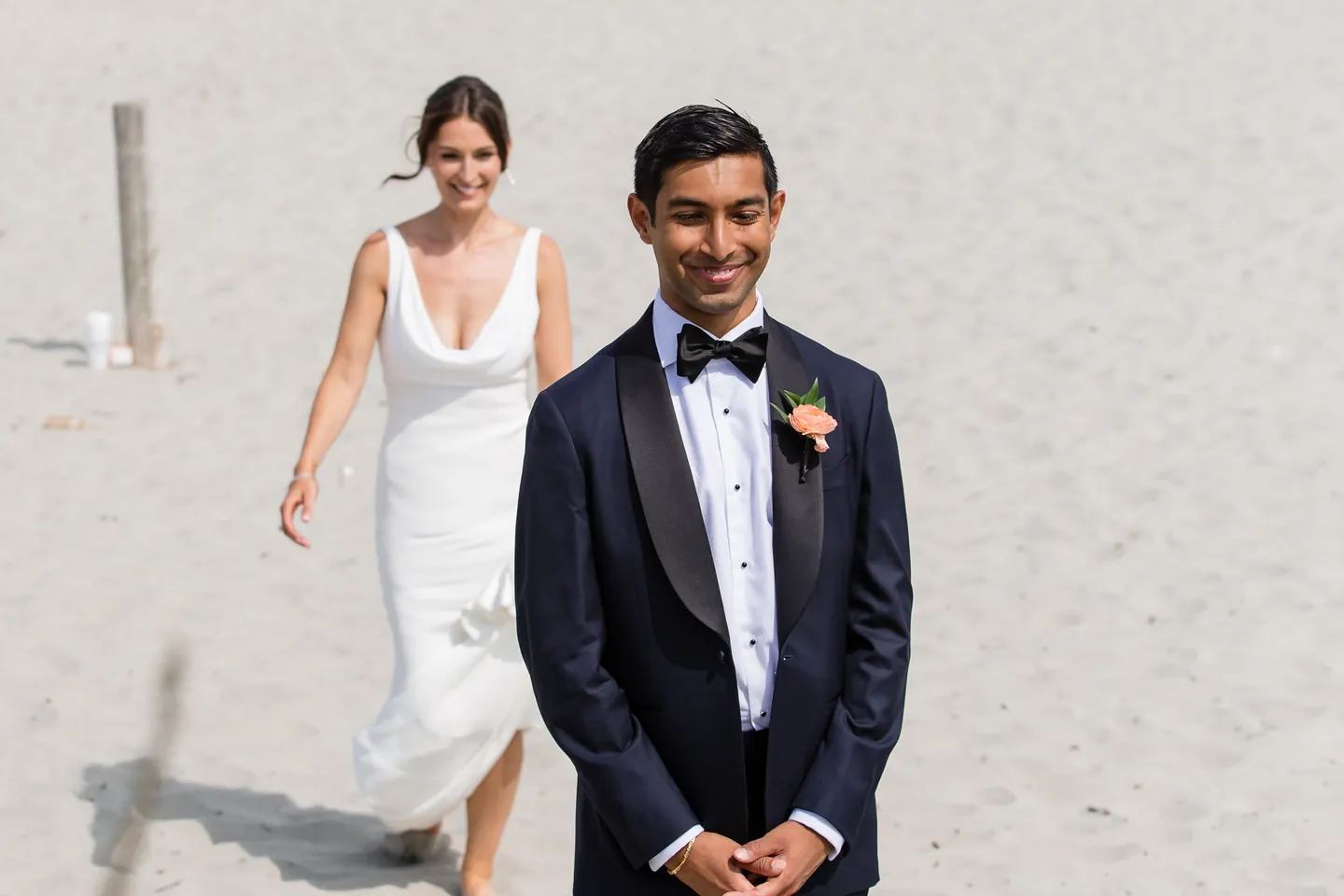 The bride walks up to the groom on the sand, both smiling before the first look