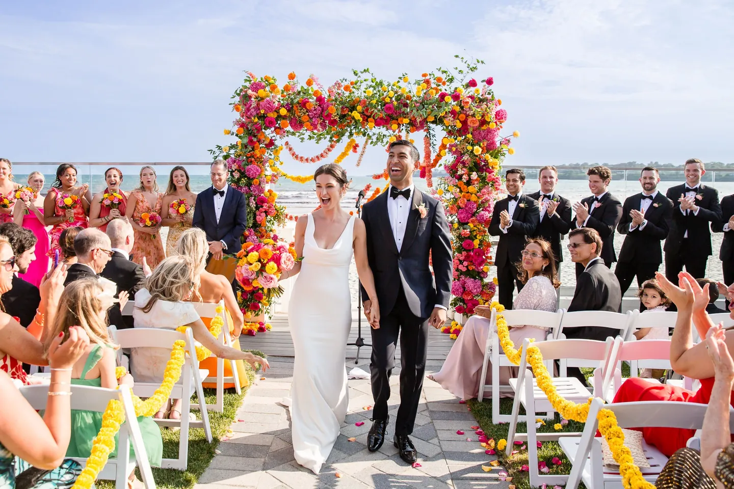 Zoey and Akshay walk back down the garland-lined aisle past standing guests