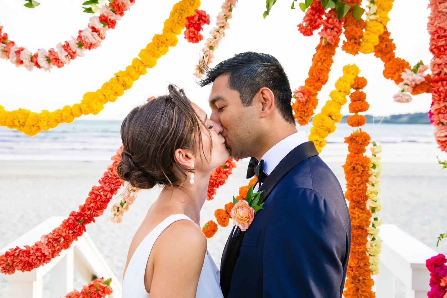 Zoey and Akshay kiss framed by strands of marigolds swinging in the breeze