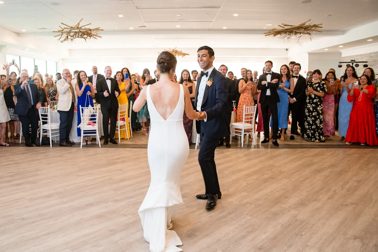 Zoey and Akshay begin their first dance on a pale wood floor ringed by guests