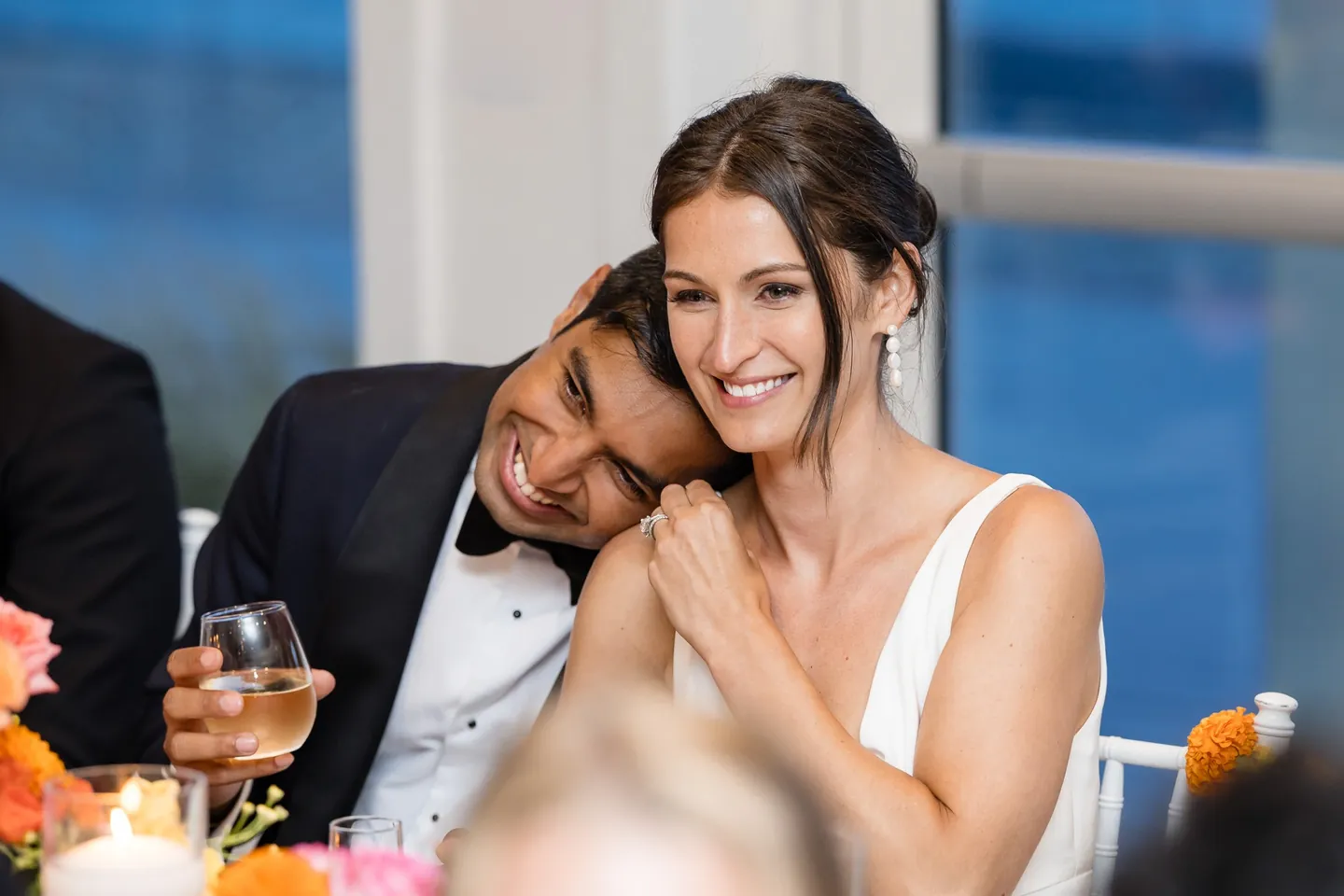 Zoey rests her head on Akshay's shoulder at the table, laughing during toasts